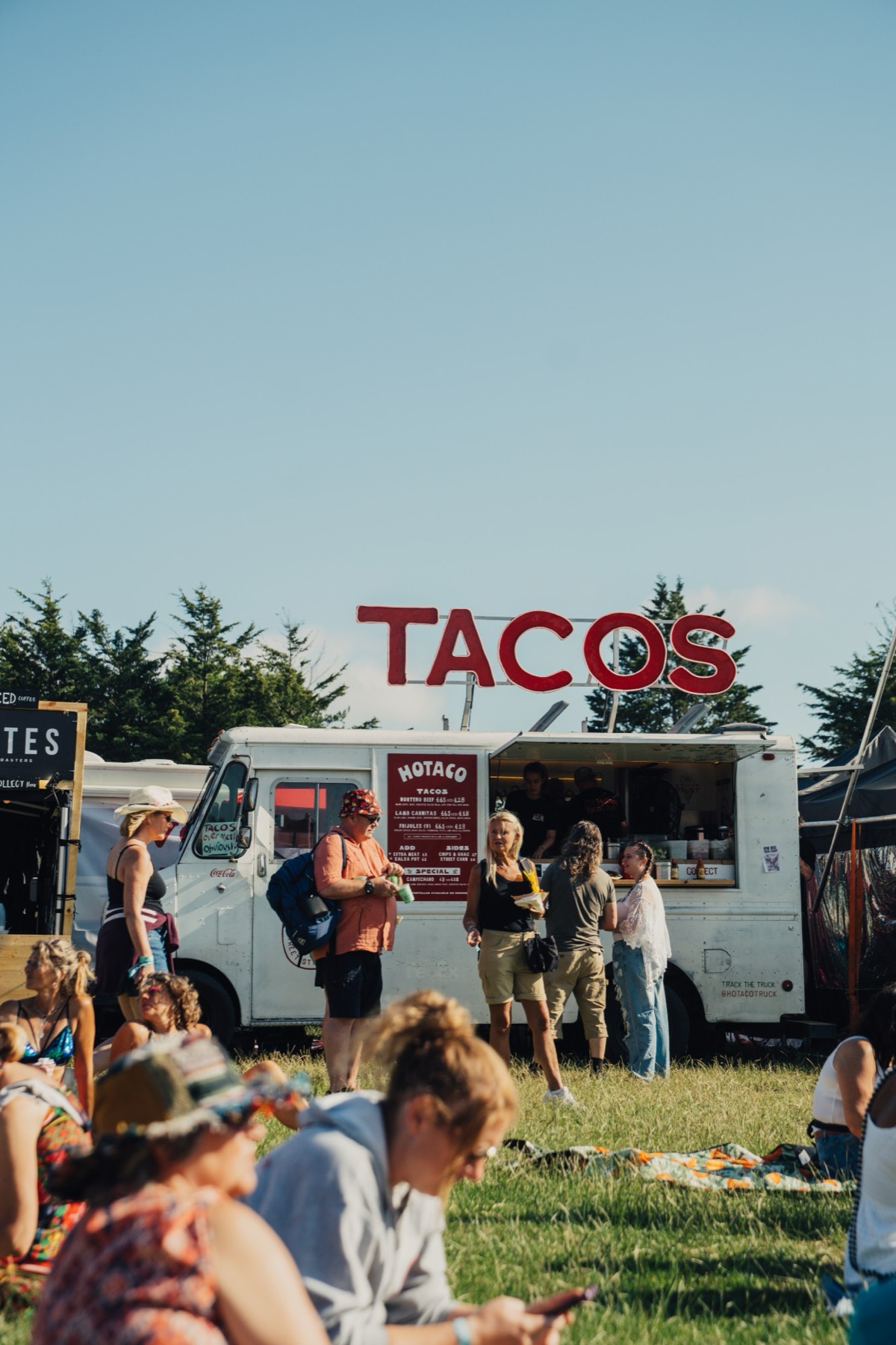 The truck in a field under the TACOS sign with a crowd sat on the grass.