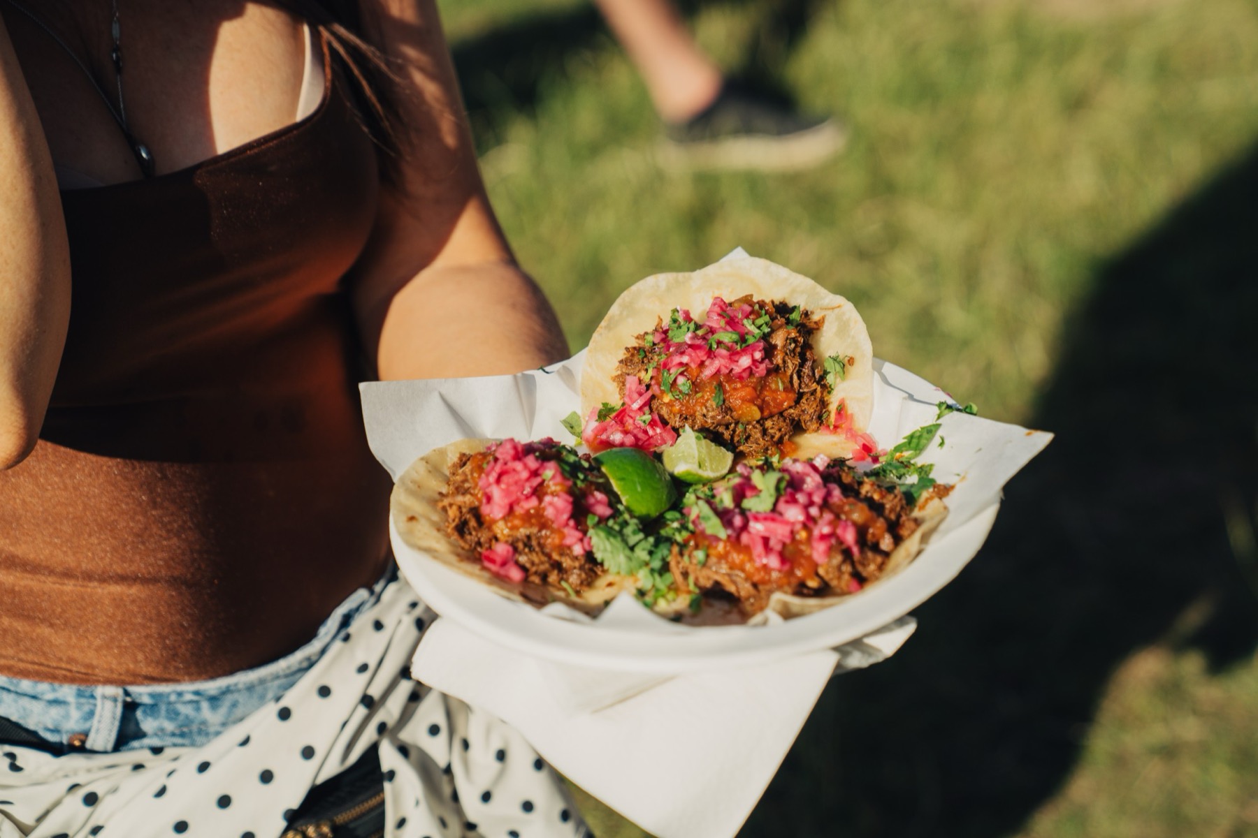 Three tacos on a plate with pickled onion, coriander and lime.