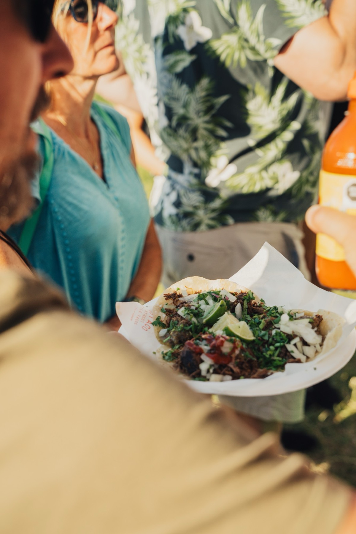 A close up of tacos being handed over, guests behind.